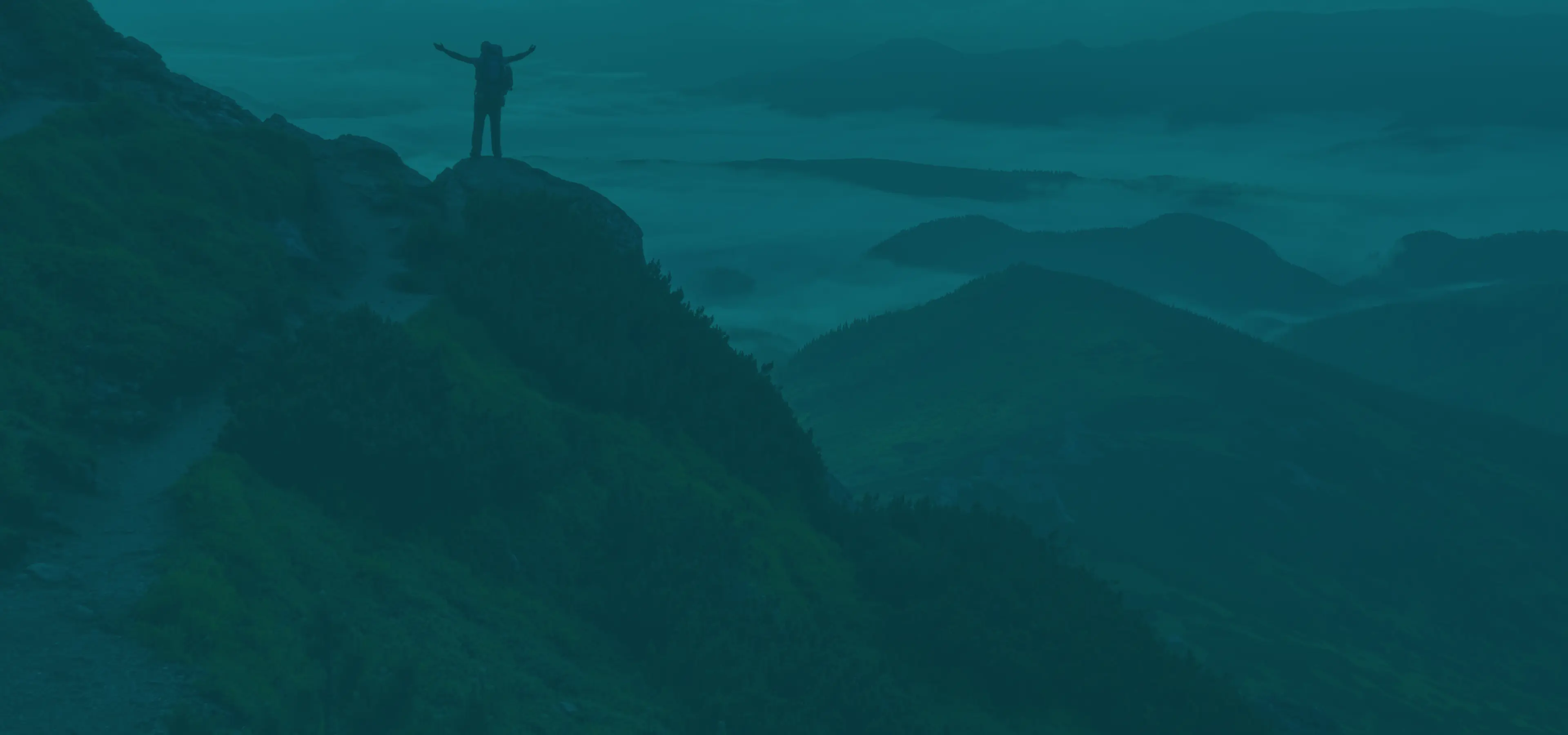 Person standing on a mountain overlooking misty valleys